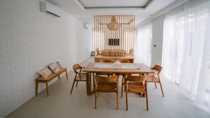 A dining area with a wooden table and chairs, a hanging light fixture, and a white brick wall. - Nyuh Lengkong Beachfront Villa (Tabanan)