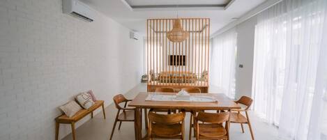 A dining area with a wooden table and chairs, a hanging light fixture, and a white brick wall.