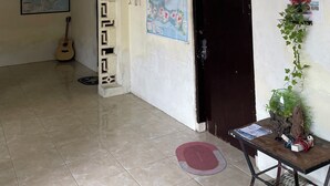 A room with a tiled floor, a black door, a map on the wall, a guitar, and a plant on a table.