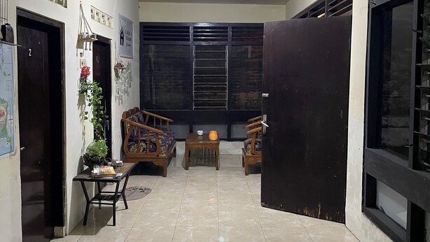 A spacious living area with a tiled floor, a sofa, a table, and a chair. There are doors and a window with blinds.