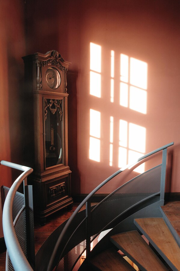 A staircase with a metal handrail and wooden steps, leading to a dark wooden cabinet with a clock. - Schloss Schmarsow (Kruckow)