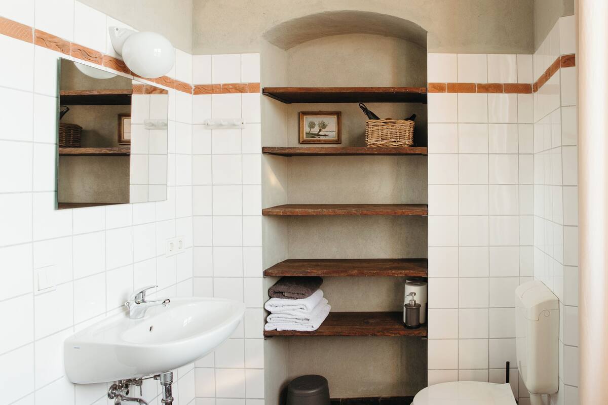 Ein Badezimmer mit Waschbecken, Holzregalen, einem Bilderrahmen und einer Toilette.