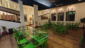 Un comedor con sillas verdes y una mesa de vidrio, pisos de madera y obras de arte en las paredes.