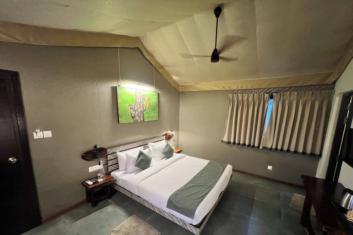 A bedroom with a bed, a nightstand, a ceiling fan, a painting, and a window with curtains.
