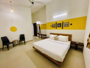 A hotel room with a bed, two chairs, a small table, a mirror, and artwork on the wall. - Kalrav Resort Pench (Kurai)