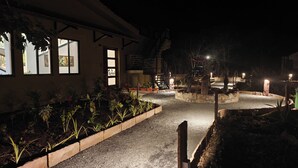 Vista nocturna de un edificio con un camino de grava, plantas en macetas y una escalera que lleva a un nivel superior.