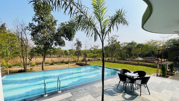Una piscina con solárium empedrado, rodeada de árboles y césped.