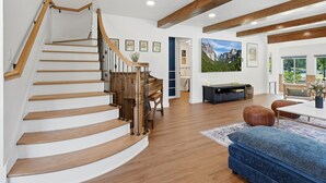 Una escalera de madera con escalones y barandilla, que conduce a una habitación con una cama, un escritorio y un ventanal grande.