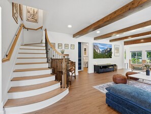 Un escalier avec des marches en bois et une rampe en bois, menant à une pièce comprenant un lit, un bureau et une grande fenêtre.