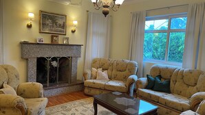 Una sala de estar con chimenea, dos sillones, un sofá, una mesa de centro de vidrio y una araña.