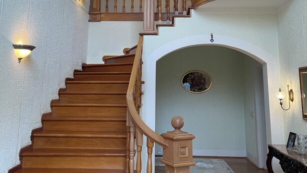 Una imponente escalera con barandillas de madera y un candelabro, que lleva a un nivel superior.