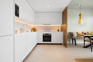 Eine moderne Küche mit weißen Schränken, einem eingebauten Ofen und einem Essbereich mit einem Holztisch und Stühlen.