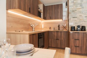 A modern kitchen with wooden cabinetry, a built-in dishwasher, and a stone backsplash. - Sommet - Cozy | 5 guests | Central | Mont-Blanc View (Chamonix-Mont-Blanc)