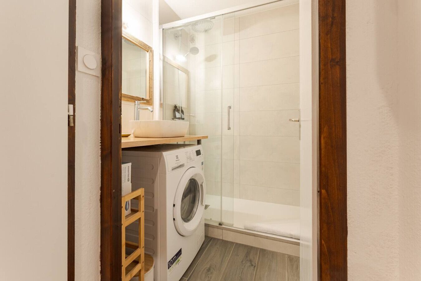 Un bagno compatto con lavatrice, box doccia in vetro e ripiano in legno.