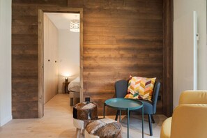 A cozy room with a wooden wall, a round table, a blue chair, a yellow chair, and a small stool. - Sommet - Cozy | 5 guests | Central | Mont-Blanc View (Chamonix-Mont-Blanc)