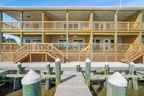 A multi-story building with balconies, a wooden deck, and a staircase leading to the upper levels. - Channel Winds | Waterfront Bliss w/ Lighthouse Views! (Chincoteague Island)