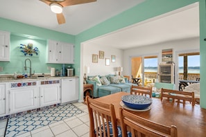A kitchen with white cabinets, a dining table with chairs, a blue patterned bowl, and a ceiling fan. - Channel Winds | Waterfront Bliss w/ Lighthouse Views! (Chincoteague Island)