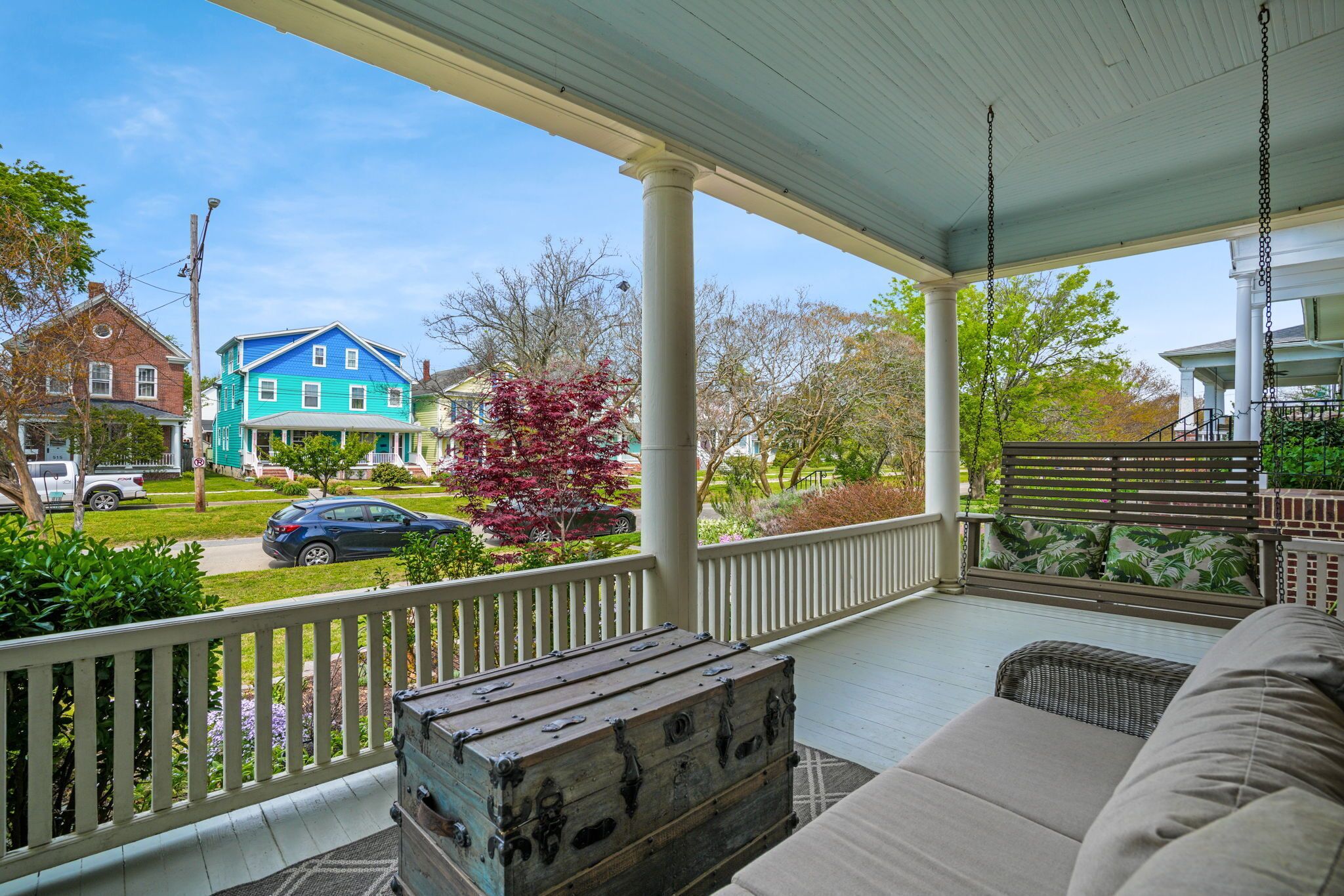 A covered porch with a white railing, a wooden bench, and a vintage trunk.