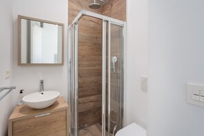 A bathroom with a wooden vanity, a white sink, a glass shower enclosure, and a mirror on the wall.