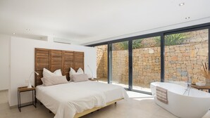 A modern bedroom with a large bed, a built-in bathtub, and a stone wall outside. - Villa lussuosa e all'avanguardia con splendida vista (Dénia)