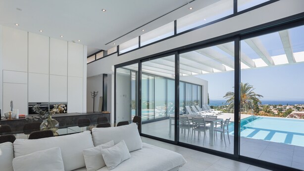 A modern living room with a large sofa, a dining area, and a view of a pool and ocean. - Villa lussuosa e all'avanguardia con splendida vista (Dénia)
