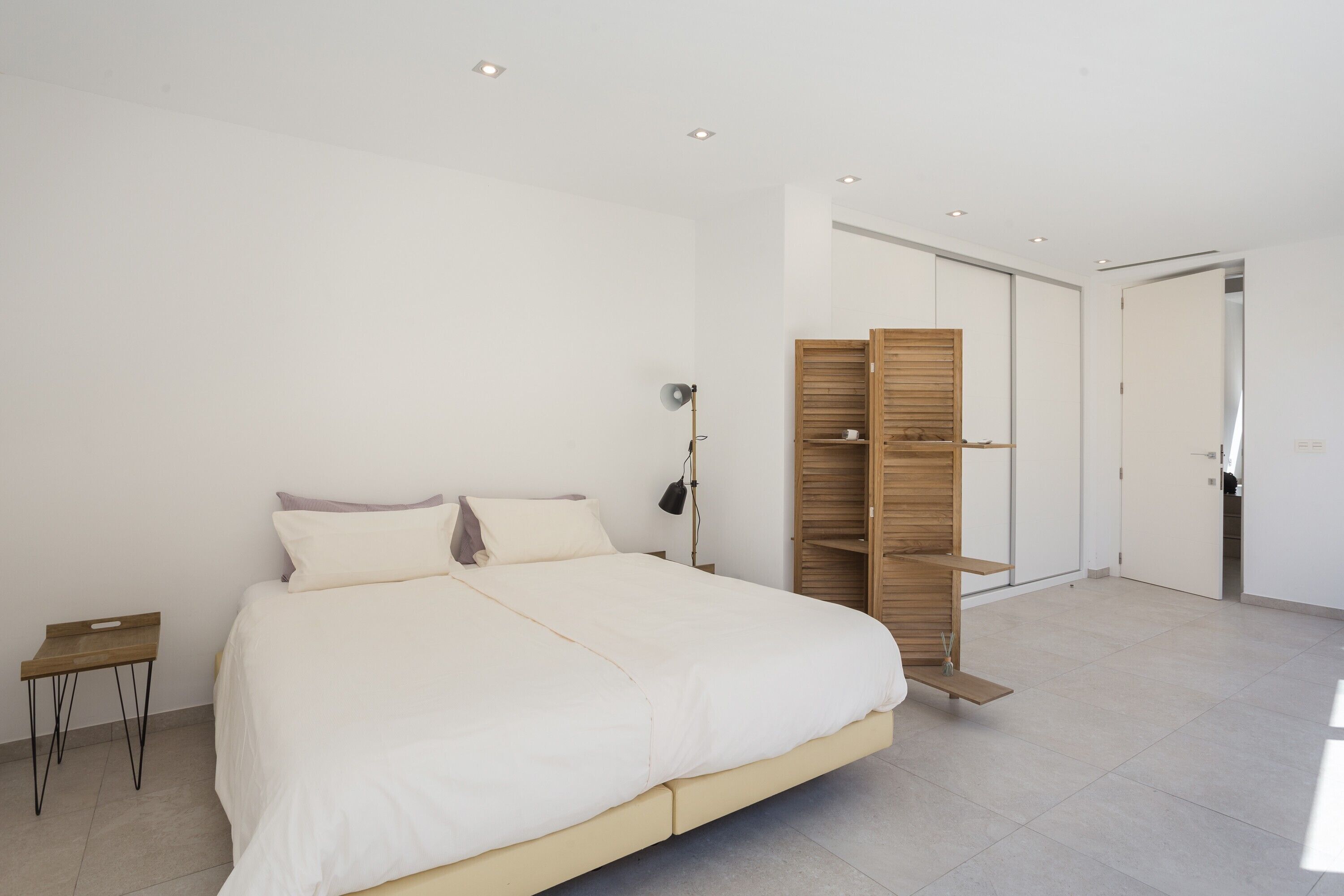 Un dormitorio moderno con una cama grande, una mesita de noche, un armario y una puerta que da a otra habitación.