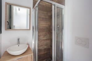 Une salle de bain avec un meuble-lavabo en bois, un lavabo blanc, un miroir et une douche Ă parois de verre.