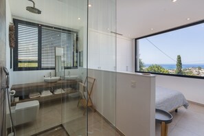A modern bathroom with a glass shower enclosure, a large window with blinds, a sink, and a toilet.