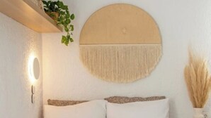 Un lit avec une literie blanche, une décoration murale ronde, une lampe fixée au mur et une petite table de chevet avec un vase.