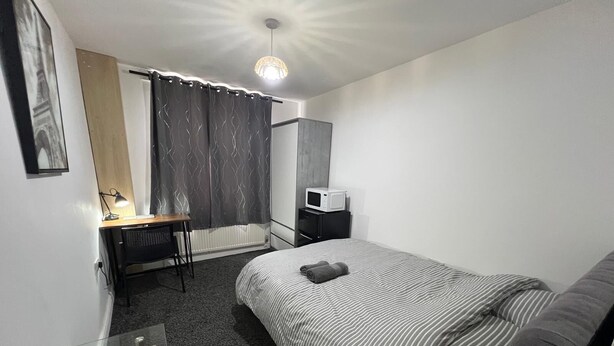 Habitación de hotel con cama, escritorio con lámpara, microondas y ventana con cortinas.