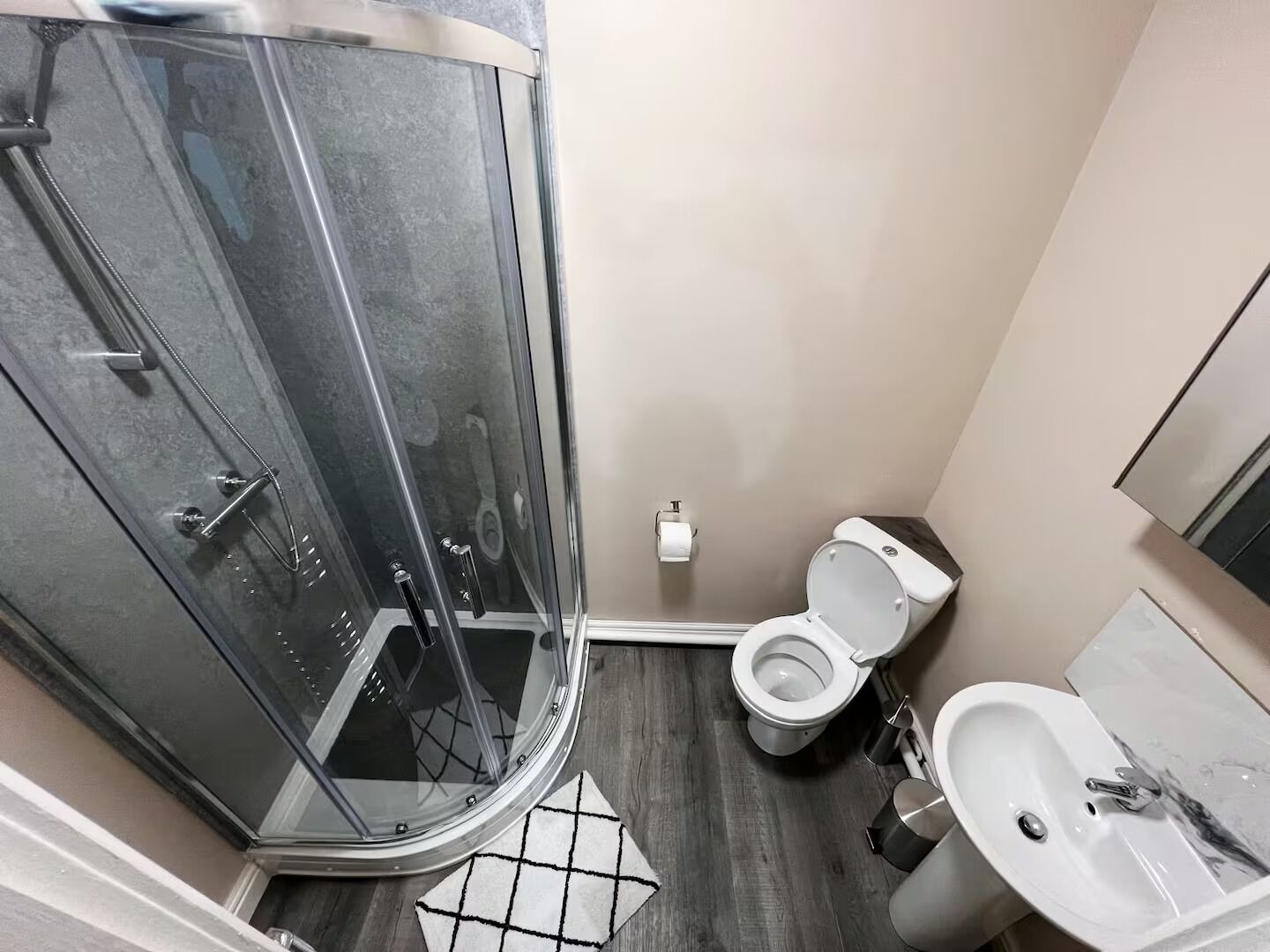 A bathroom with a glass-enclosed shower, a toilet, and a sink.