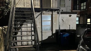 Una escalera que lleva a un edificio con una puerta de garaje, un coche aparcado y un pequeño espacio al aire libre con suelo de hormigón.