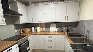Una cocina compacta con armarios blancos, encimera de madera, horno empotrado, lavadora y lavamanos.