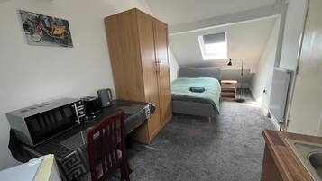 A compact room with a bed, a desk with a computer, a chair, a wardrobe, a radiator, and a window.