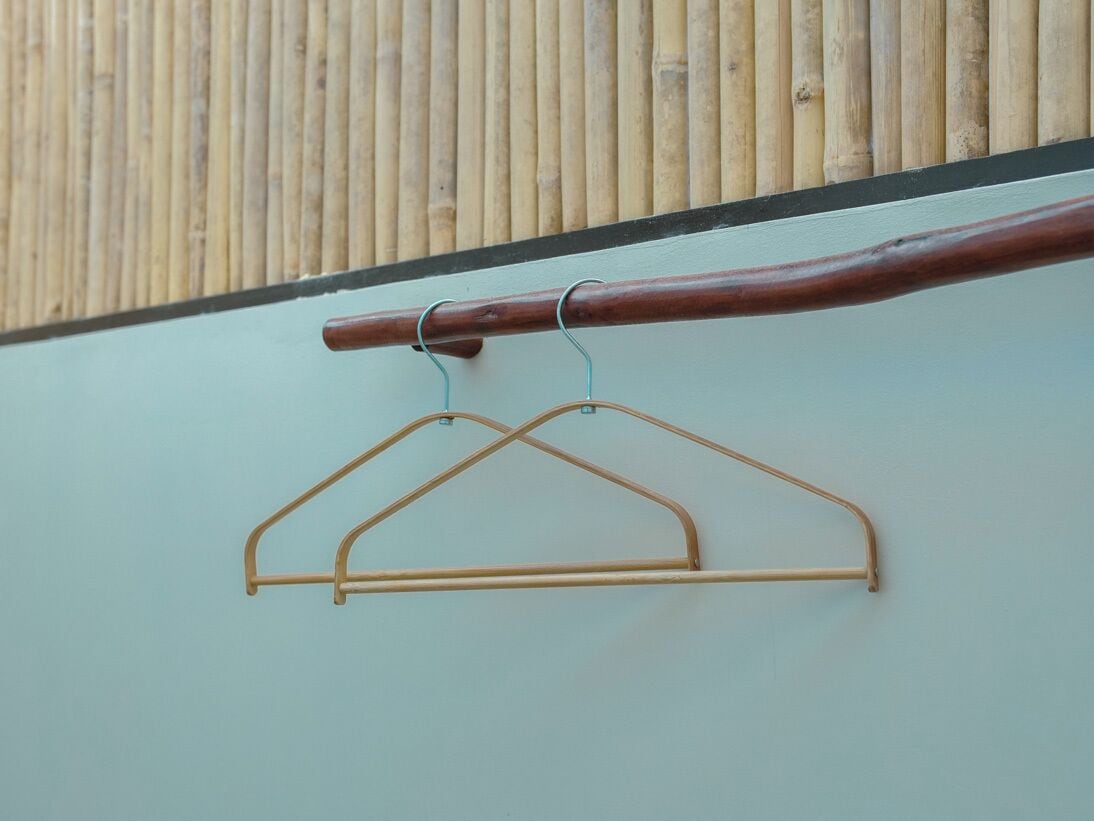 A wooden handrail with metal hooks and a metal hanger against a wall.