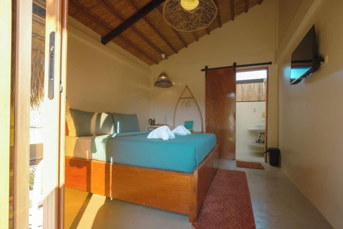 Un dormitorio con cama de madera, un escritorio pequeño, una silla, un televisor y una ventana con cortinas.