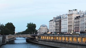 Une rivière bordée de bâtiments, un pont et une structure en forme de dôme en arrière-plan.