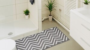 Une salle de bain moderne dotée d’une douche, de toilettes et d’un lavabo, avec des carreaux blancs et un tapis à motifs chevrons.