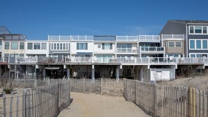 Ein Hotel direkt am Strand mit mehreren Balkonen, einem Sandweg und einem Holzzaun.