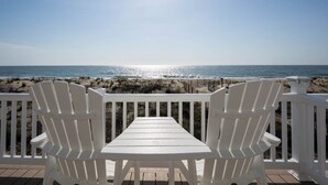 Eine Terrasse mit weißen Stühlen und einem Tisch mit Blick auf den Strand.