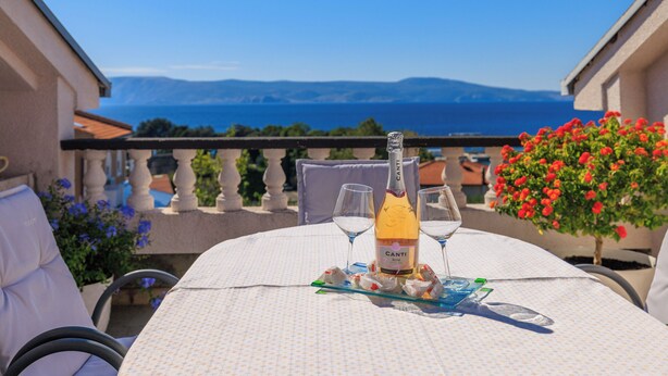 Une table avec une bouteille de vin Canti Rosé, deux verres et une assiette de collations, le tout placé sur un balcon offrant une vue panoramique.