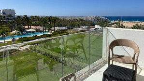 A balcony with a view of a pool, palm trees, and a beach.