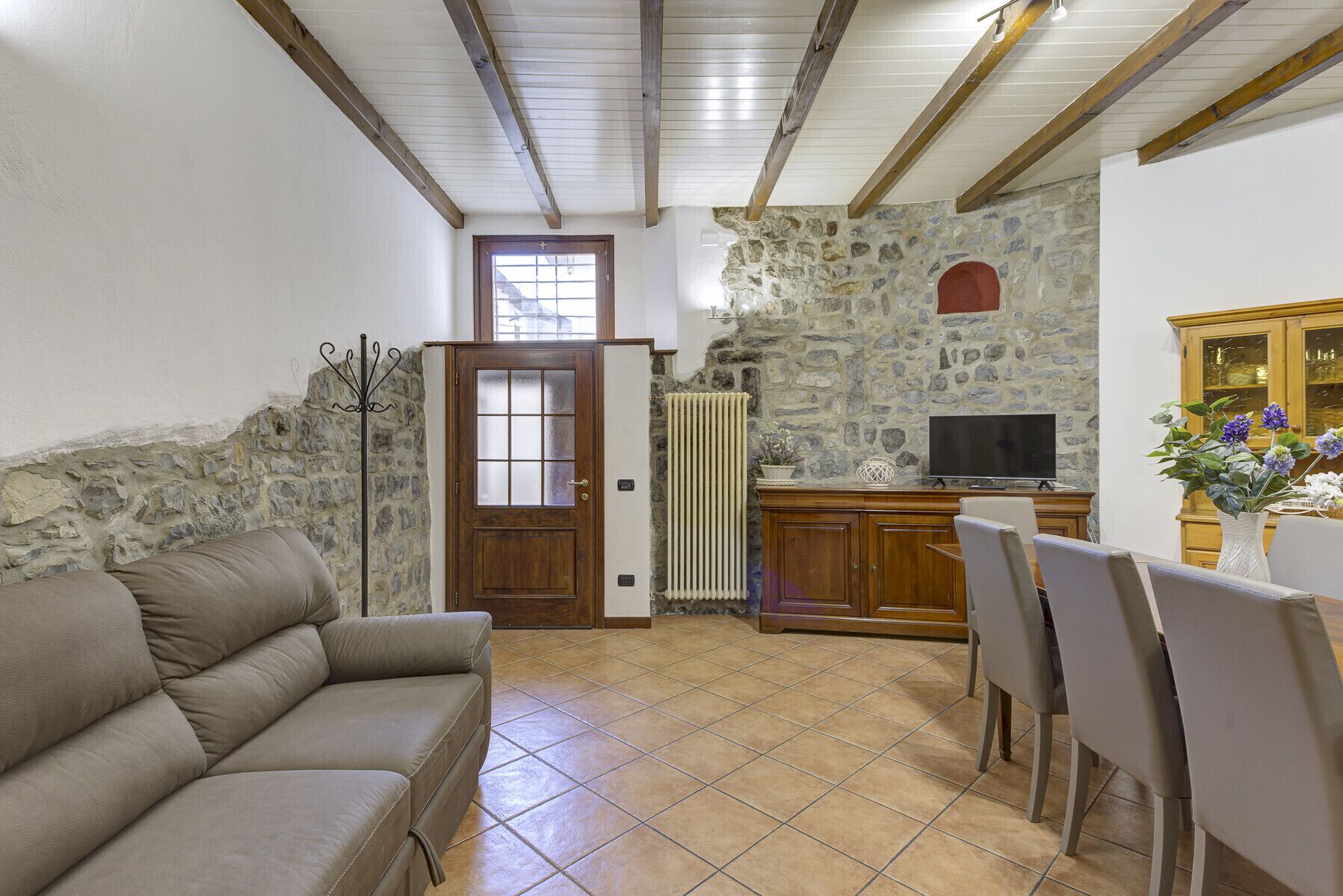 A living room with a sofa, a TV, a stone wall, and a wooden cabinet.