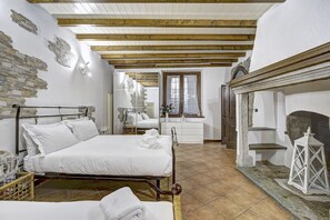 Ein Zimmer mit Bett, Nachttisch, Spiegel, Fenster mit Vorhängen, Kamin und Wandverkleidung aus Stein.