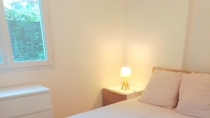 Et soveværelse med en seng, et natbord med lampe, et vindue og en hvid kommode.