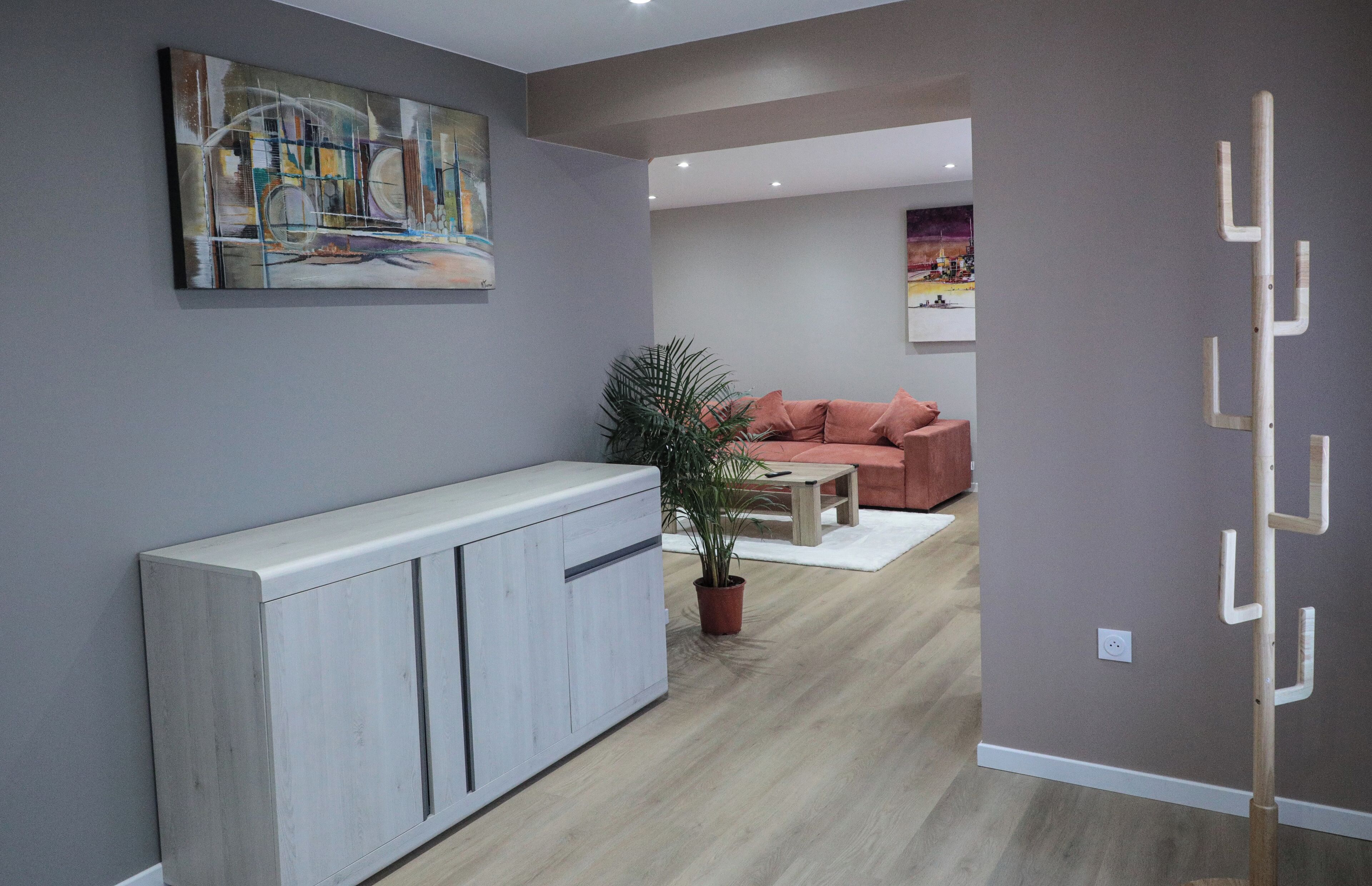 A modern living room with a grey sofa, a white cabinet, a potted plant, and a painting on the wall.