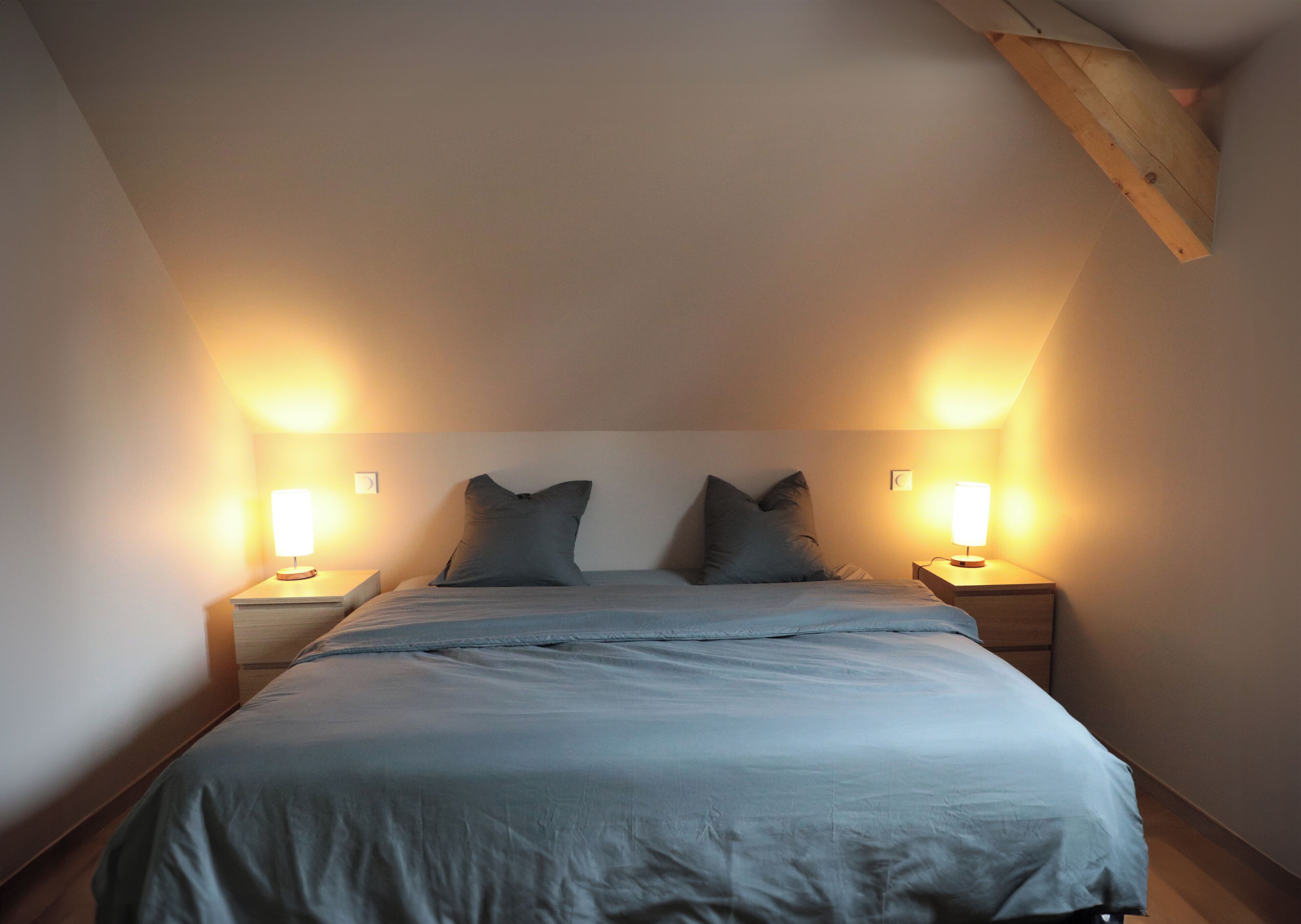 A bedroom with a bed, two bedside lamps, and a sloped ceiling.