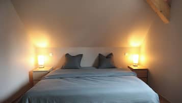A bedroom with a bed, two bedside lamps, and a sloped ceiling.