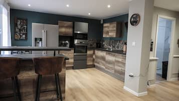 A modern kitchen with a central island, bar stools, stainless steel appliances, and a clock on the wall.