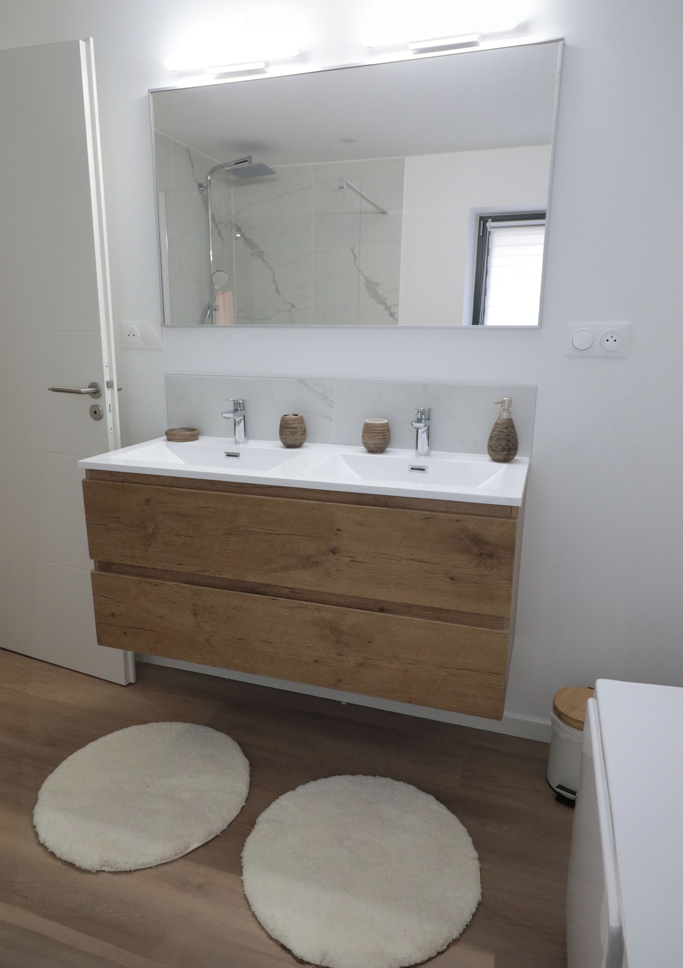 A bathroom with a white sink, wooden vanity, two round rugs, and a large mirror.